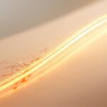 An abstract image of a golden-orange wave washing over a dull surface, symbolizing how Vitamin C for skin brightens and renews the complexion