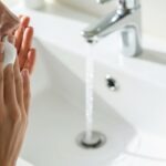 Best facial cleansers for anti-aging being applied with foam over bathroom sink with running water